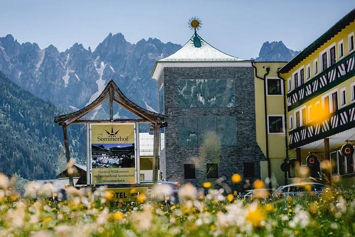 Hotel Sommerhof in den österreichischen Alpen mit Blumenwiese und Gebirgskulisse im Hintergrund