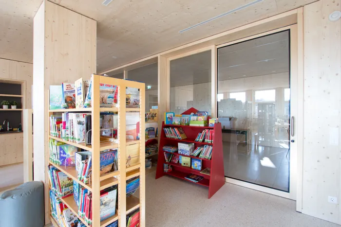 Helle Kinderecke mit Bücherregalen voller bunter Kinderbücher in Holzraum mit Glastür