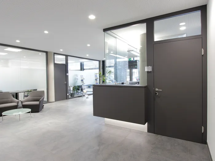 Moderne Empfangshalle mit grauem Tresen, Glastüren und Wartebereich mit Sesseln