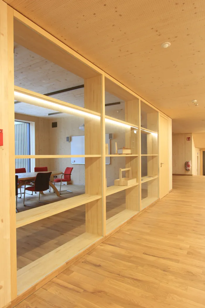 Moderner Konferenzraum mit Holzwänden, Glastrennwand und roten Stühlen in heller Büroeinrichtung