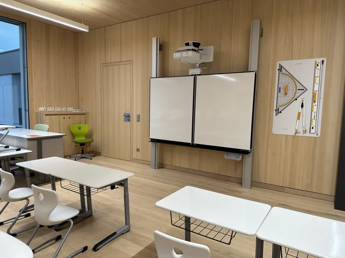 Moderner Klassenraum mit interaktivem Whiteboard, Schülertischen und geometrischem Lehrmittel an der Wand