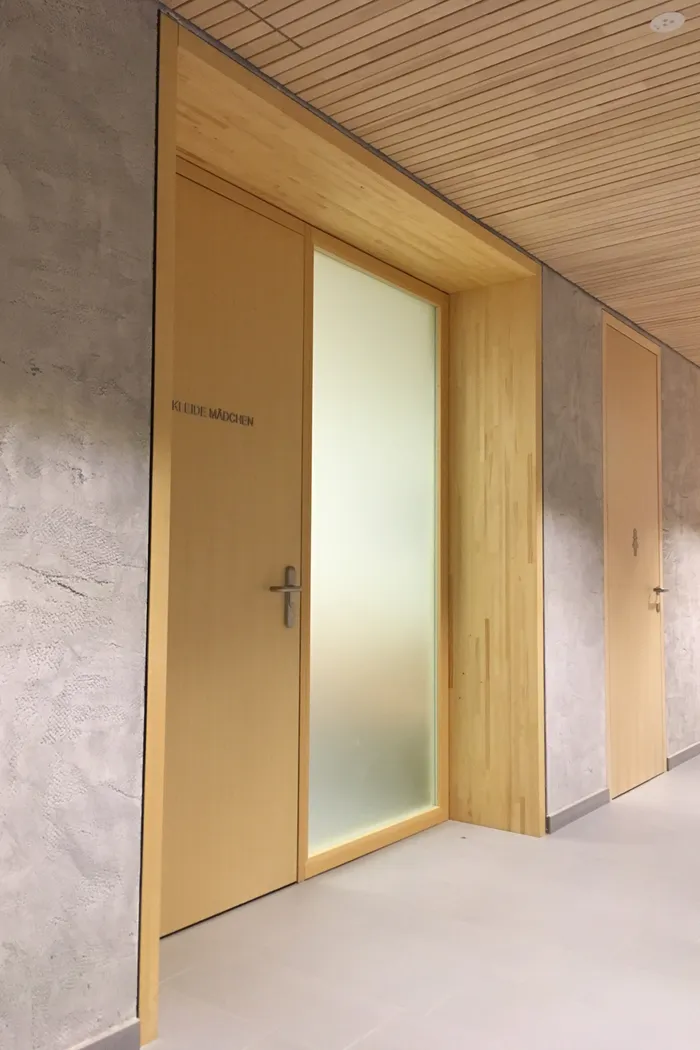 Holztür mit der Aufschrift 'KLEIDE MÄDCHEN' in einem modernen Innenflur