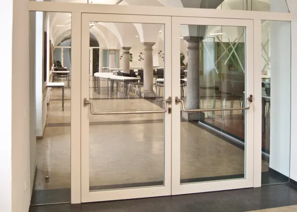 Moderne Glastür mit Blick auf einen hellen Konferenzraum mit Gewölbedecke und Säulen