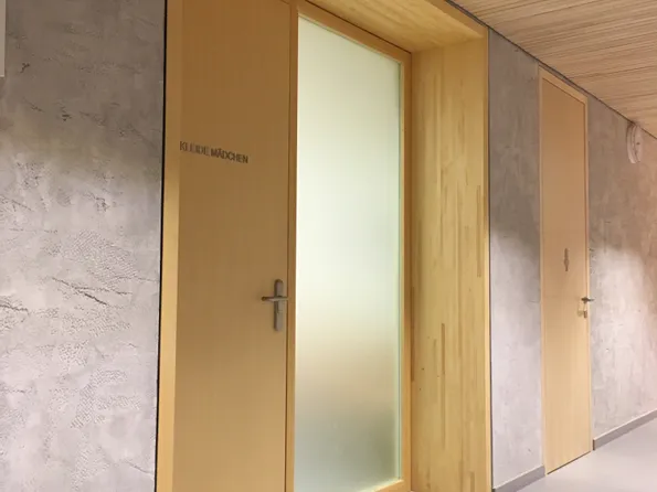 Holztür mit der Aufschrift 'KLEIDE MÄDCHEN' in einem modernen Innenflur