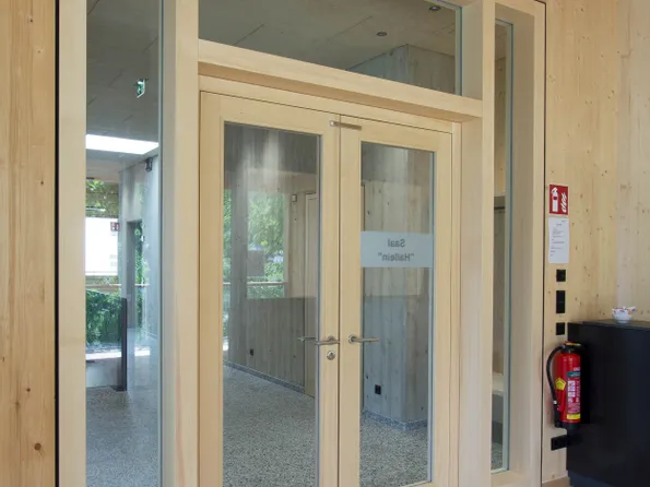 Moderne Glastür mit Holzrahmen in einem öffentlichen Gebäude mit Notausgangsschild