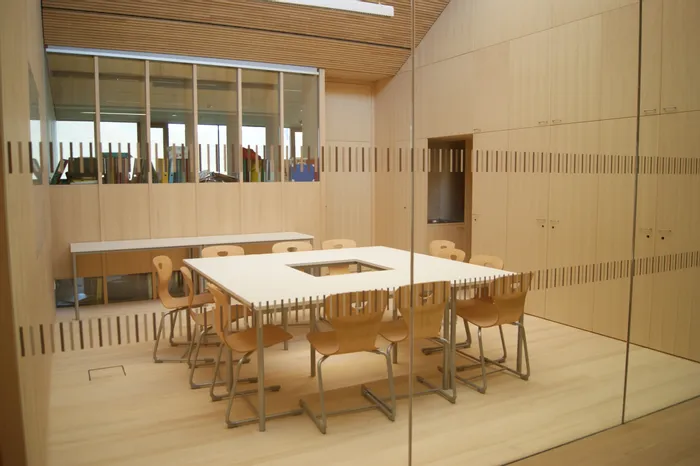 Moderner Besprechungsraum mit Holzmöbeln, quadratischem Tisch und Stühlen in schulähnlicher Umgebung