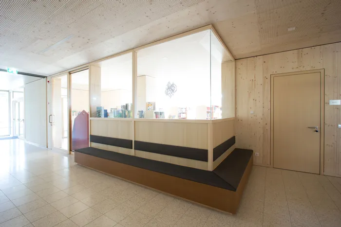Helle Bibliothek mit moderner Holzverkleidung und Sitzbank vor verglastem Bücherraum