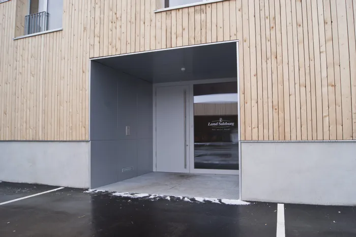 Eingang eines modernen Gebäudes mit Holzfassade und Glastür, Beschriftung Land Salzburg