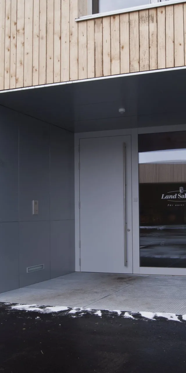 Eingang eines modernen Gebäudes mit Holzwand und Tür mit Aufschrift Land Salzburg