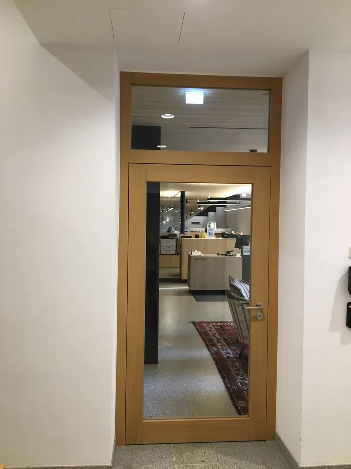 Holztür mit Glasfenster zeigt Rezeption und Wartebereich mit Teppich im Büro