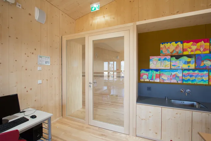 Heller Innenraum mit Holzwänden, Kindermalereien über Spüle und Glastür zu Nebenraum