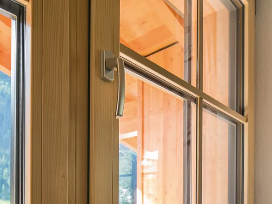 Doppelfenster aus Holz mit Metallgriffen und Blick auf einen sonnigen Balkon