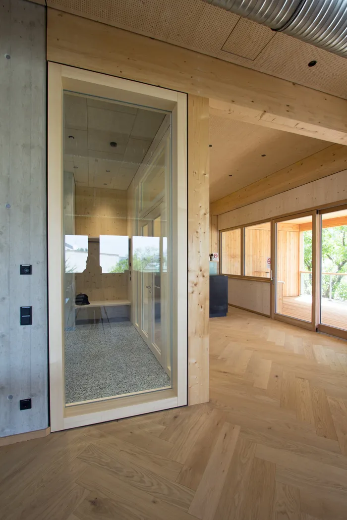 Modernes Holzinterieur mit Glaskabine, Parkettboden und großen Fenstern mit Blick ins Grüne
