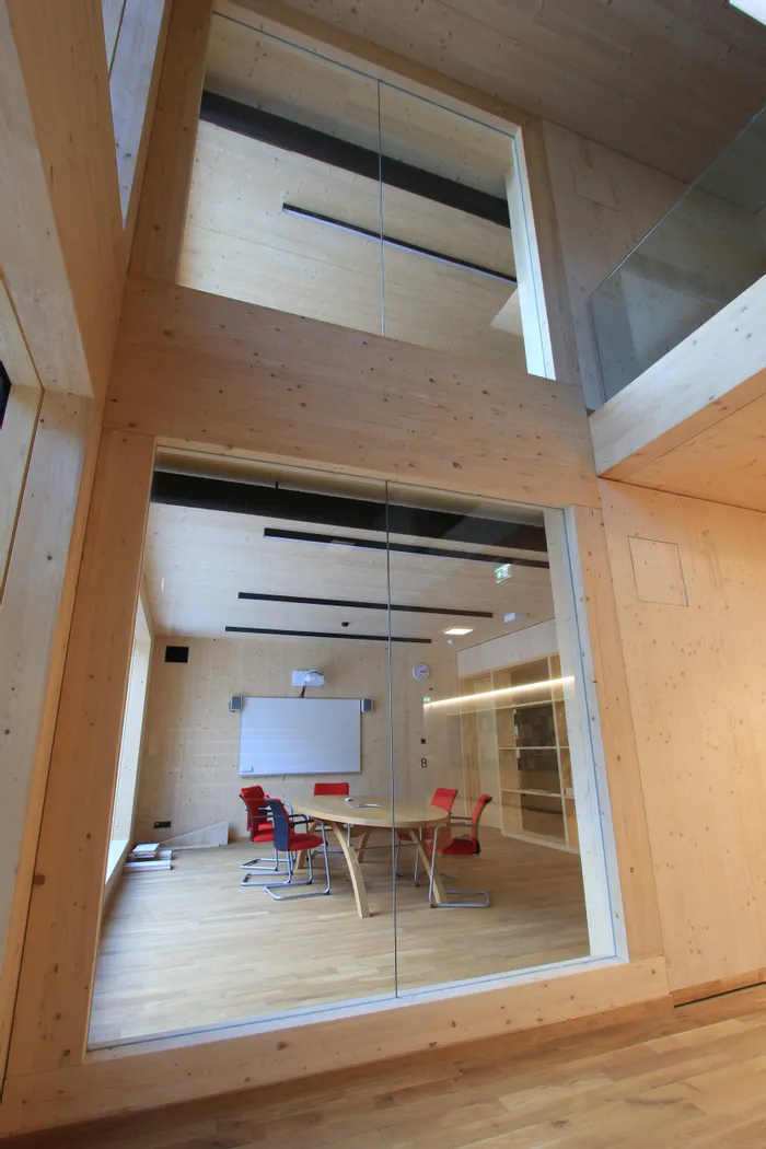 Moderner Konferenzraum mit Holzwänden, Glastür und roten Stühlen um einen Holztisch