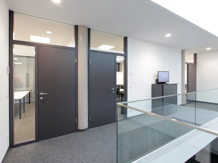 Modernes Büroflur mit grauen Türen, Glaswänden und Bildschirm auf Schrank