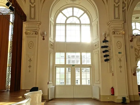 Helles Foyer mit hohen Fenstern, Kronleuchter und Holzboden in einem historischen Gebäude