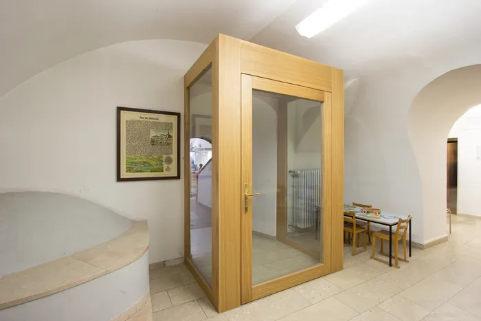 Holztelefonkabine mit Glastüren in einem hellen Flur neben Kindertisch und Stühlen