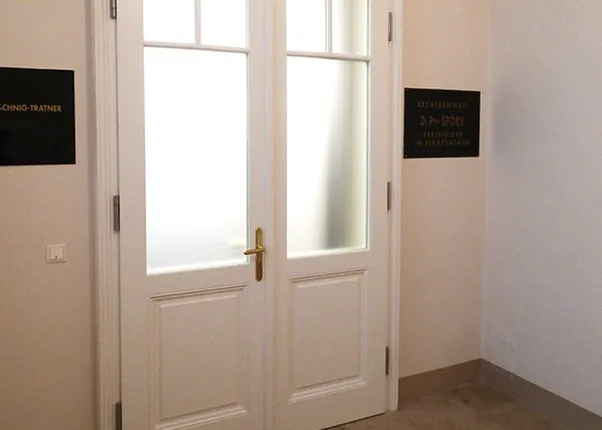 Weiße Doppeltür mit Milchglasfenstern in einem Bürogebäude mit Kanzleischildern an der Wand