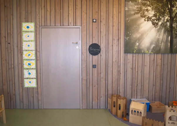 Holzwand mit Tür, Kindergemälden, Spielsachen und einem Bild mit Sonnenstrahlen im Wald