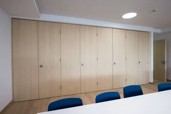Klapptürtrennwand aus hellem Holz in einem modernen Konferenzraum mit blauen Stühlen