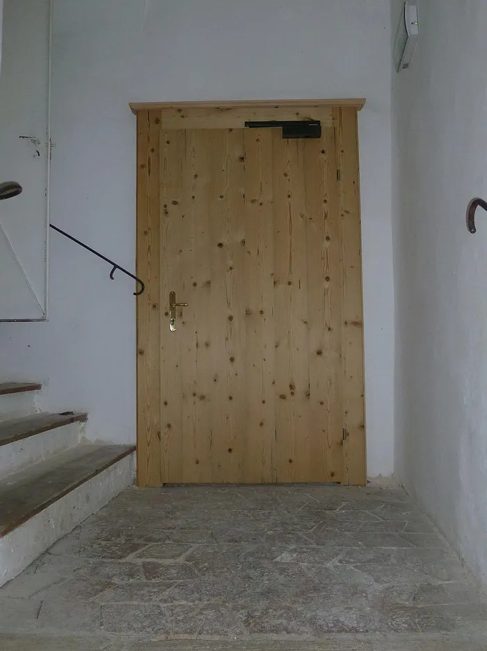 Geschlossene Holztür am Ende einer Steintreppe in einem schmalen Innenflur