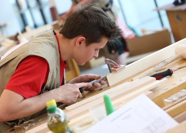 Junger Handwerker arbeitet konzentriert mit einem Stechbeitel an einem Holzstück in der Werkstatt