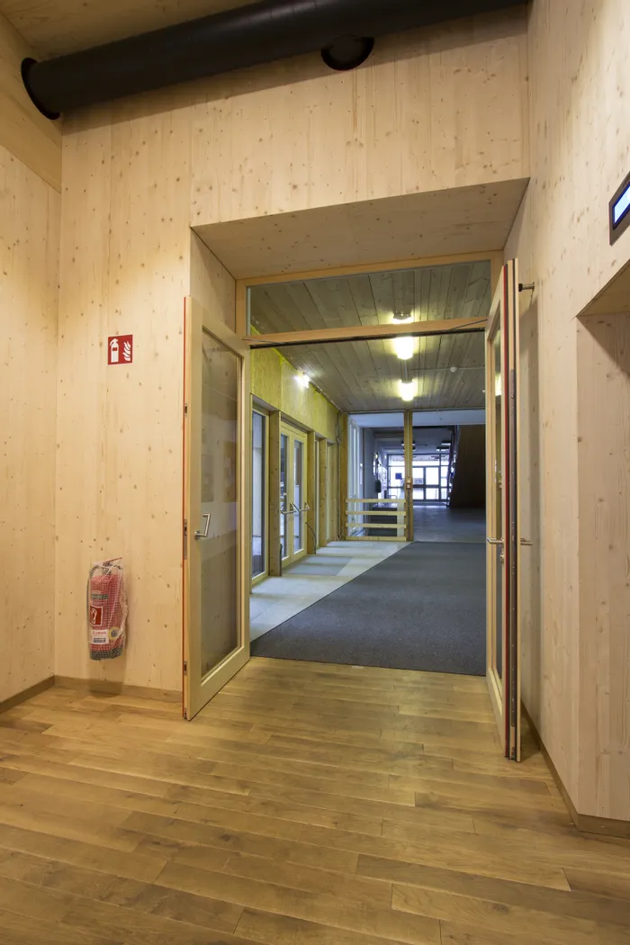 Innenraum eines modernen Gebäudes mit Holzwänden, geöffneten Glastüren und Blick auf einen Flur