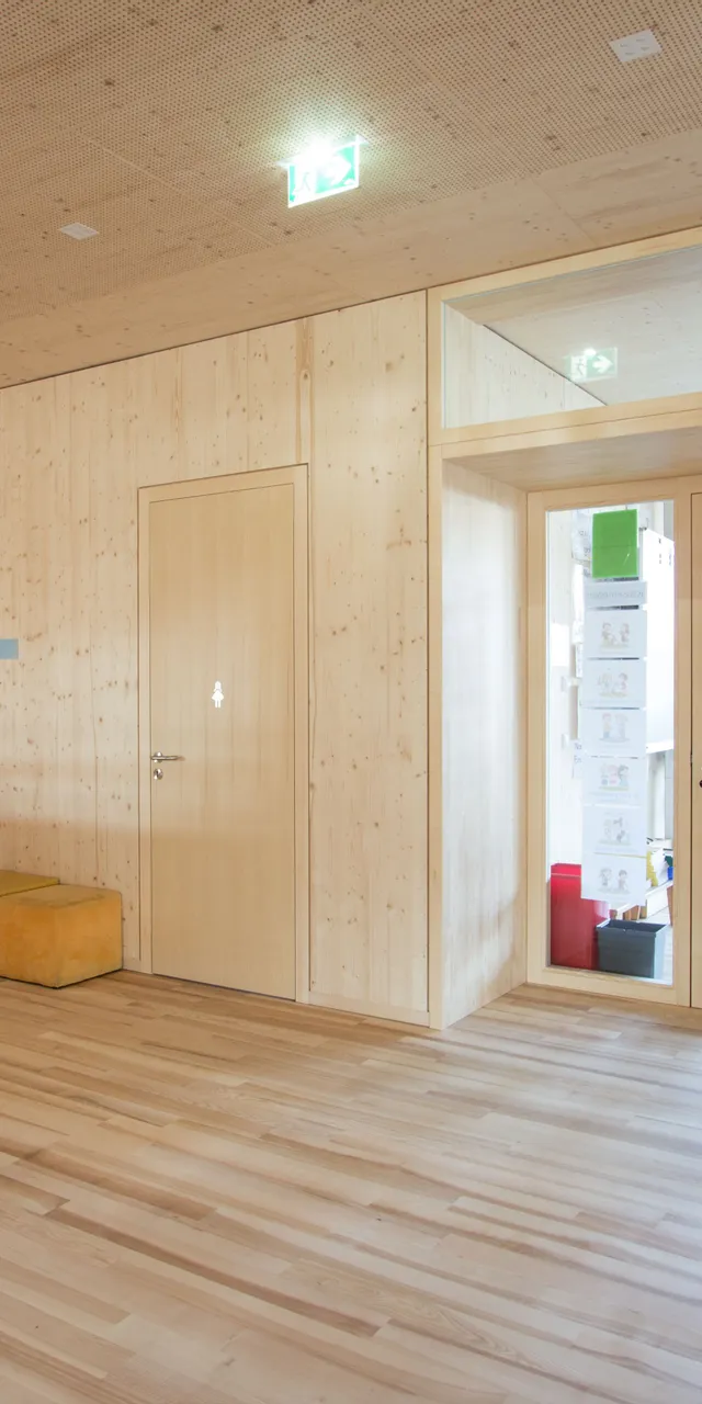 Heller Flur in einer Grundschule mit Holzwänden, Kinderzeichnungen und Garderobe