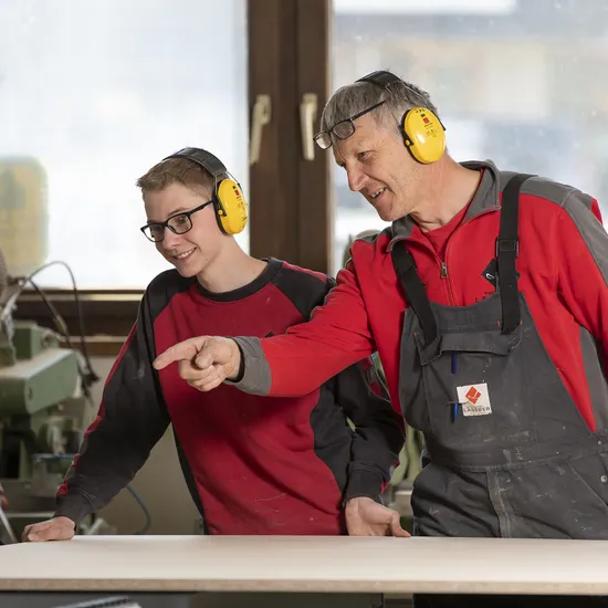 Ausbilder zeigt Auszubildendem in der Schreinerei Arbeitsschritte an einer Werkbank