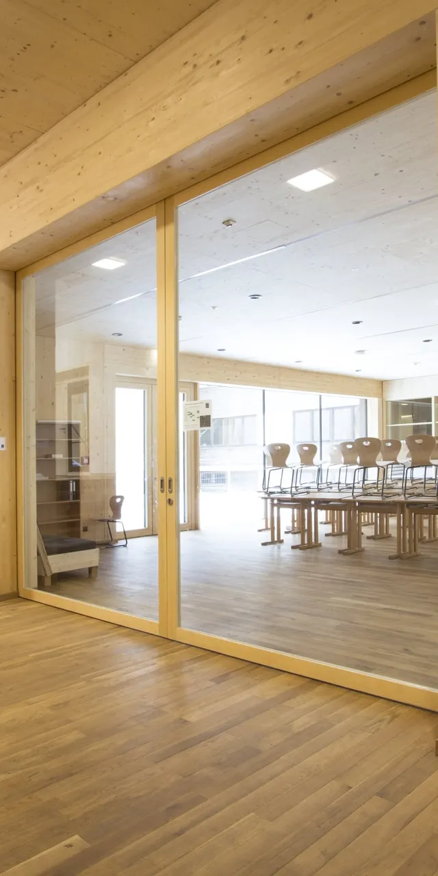 Moderner Schulflur mit Holzverkleidung und Blick in ein leeres Klassenzimmer mit gestapelten Stühlen