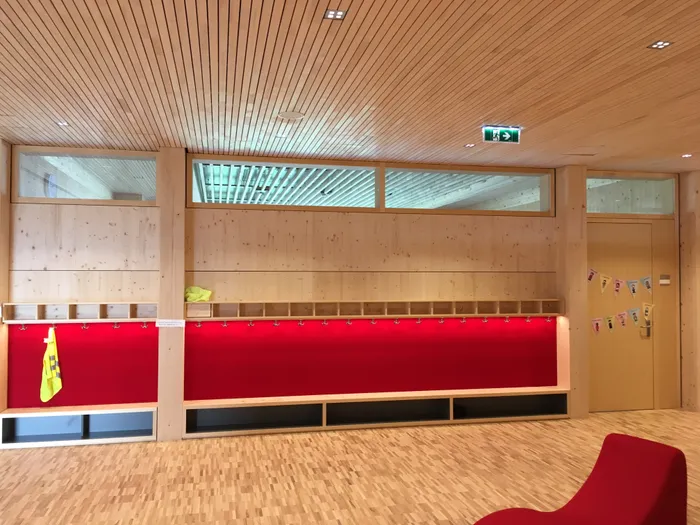 Moderne Garderobe mit roten Wänden und Holzverkleidung in einem Kindergarten oder Schulflur