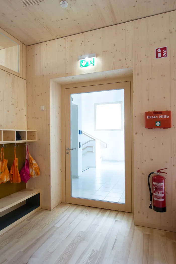 Holzflur mit Glastür, Erste-Hilfe-Kasten, Feuerlöscher und Notausgangsschild