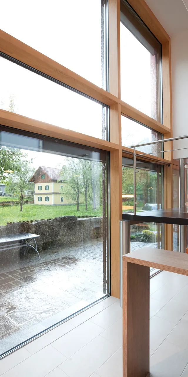 Moderne Holztreppe mit großen Panoramafenstern und Blick auf regnerischen Garten