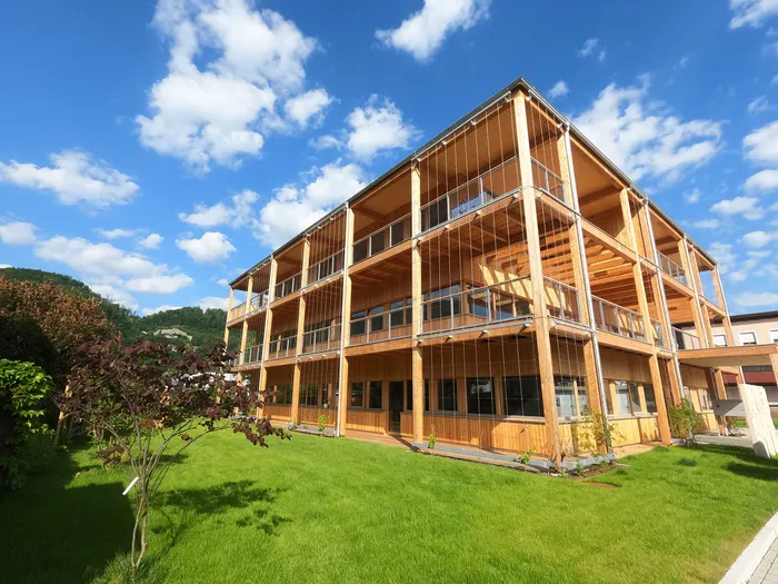 Modernes Holzwohnhaus mit großen Balkonen und Grünfläche bei sonnigem Wetter