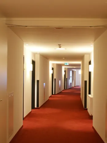 Modern hotel hallway with red carpet and white walls under warm lighting