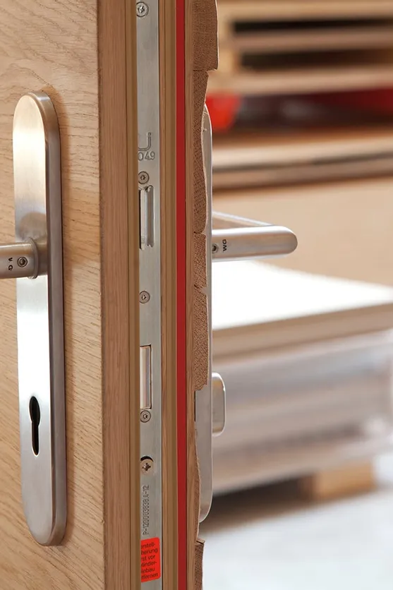 Detail einer geöffneten Holztür mit Edelstahl-Türklinken und eingebautem Sicherheitsschloss