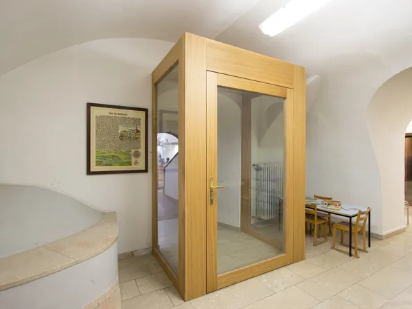 Holztelefonkabine mit Glastüren in einem hellen Flur neben Kindertisch und Stühlen