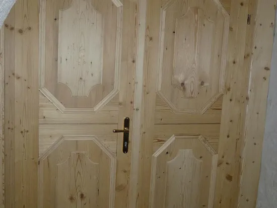 Doppelflügelige Holztür mit geschnitzten Paneelen unter einem gemauerten Torbogen