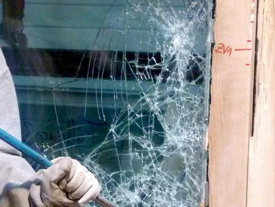 Hand mit Handschuh entfernt zerbrochenes Sicherheitsglas aus einem Holzfensterrahmen mit Brecheisen