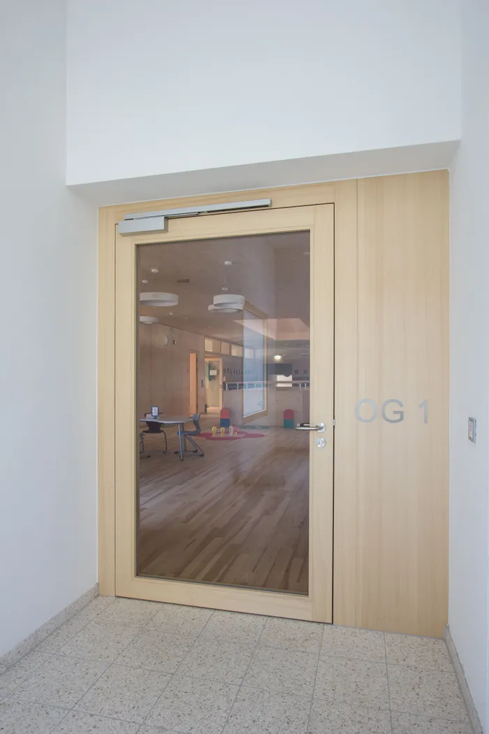 Holztür mit Glaseinsatz zu einem modernen Innenraum mit Holzfußboden und Kinderspieltischen