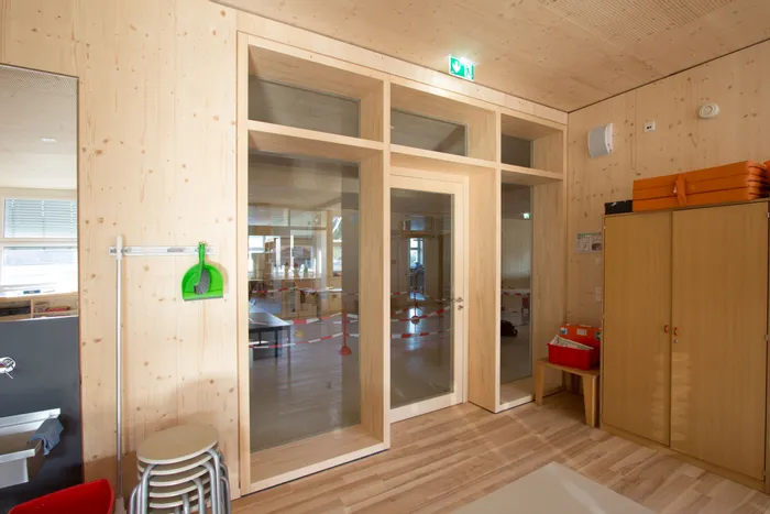 Innenraum einer modernen Kindertagesstätte mit Holzwänden, Möbeln und Glastür